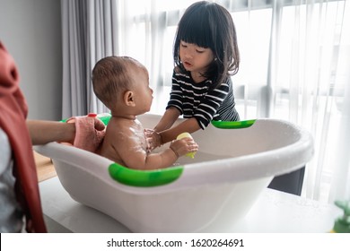 helpful sister wash her baby brother while taking a bath time in basin