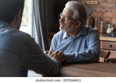 Helping hands of son. Attentive grownup kid sit at table close to sad senior hoary father touch his palms listen to problem. Young grandson give support to depressed old grandfather help overcome loss