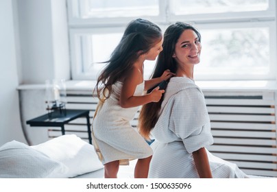 Helping to made hairstyle. Young mother with her daugher have beauty day indoors in white room. - Shutterstock ID 1500635096