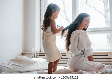 Helping to made hairstyle. Young mother with her daugher have beauty day indoors in white room. - Shutterstock ID 1500635102