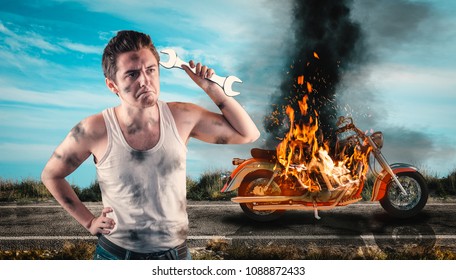 Helpless Man Holding A Wrench With His Motorcycle On Fire In The Background. Needs Help To Repair The Motorbike. 
