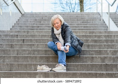 Helpless senior woman massaging her Foot to relive aches and pains after falling down steps
