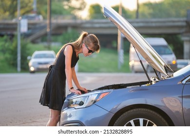 Helpless Woman Standing Near Her Car With Open Bonnet Inspecting Broken Motor. Young Female Driver Having Trouble With Vehicle