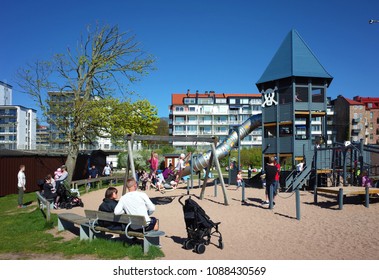 Helsingborg, Sweden - 05 May, 2018: Parents Sit On Bench While Kids Playing On Children Playground In Sunny Day, Real People In Everyday Life