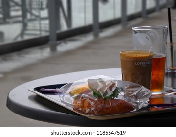 HELSINKI, FINLAND - AUGUST 20, 2018: Ham Croissant Sandwich In Transparent Plastic Packaging And Coffee And Beer In Glasses On Tray On Round Table On The Open Terrace Of Helsinki Port Terminal