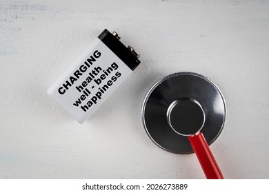 Helth, Well Being And Happiness Concept. Battery And Doctor's Stethoscope On A White Wooden Background.