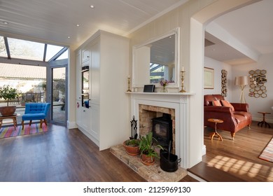 Hemmingford Grey, Cambridgeshire - Feb 10 2018: Stylish luxury kitchen with fireplace and woodburner stove on brick hearth open to sitting room lounge on one side and window overlooking garden patio - Shutterstock ID 2125969130