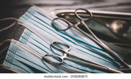 Hemostatic Forceps scissors on top of surgical face masks in a stainless steel tray close-up photograph.