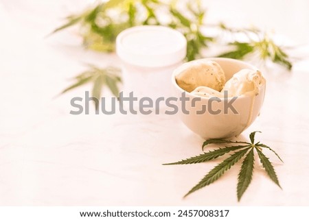 A hemp leaf is lying on a mock-up jars of ice cream on a white marble table. Green cannabis leaves on the background. Organic food and health.