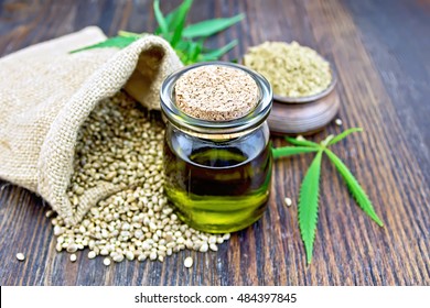 Hemp oil in a glass jar with flour in a clay bowl and grain in a bag, cannabis leaves and stalks on a wooden boards background