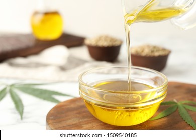 Hemp oil pouring from sauce boat into bowl on table