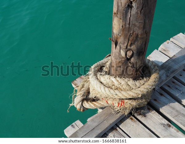The hemp rope is rolling on the wooded pier beside\
wood bridge near the sea.