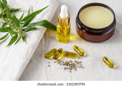 Hemp salve balm and relaxing CBD serum oil bottle and capsules as a complex in the homeopathy  treatment  with cannabis plant and seeds on fabric. Cannabis products - Shutterstock ID 2101393795
