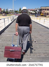 Henley Beach, South Australia - December 2009: An Old Man Carrying His Fishing Gears Looking For The Next Fishing Spot At Henley Beach Jetty, South Australia On A Bright Summer Day.