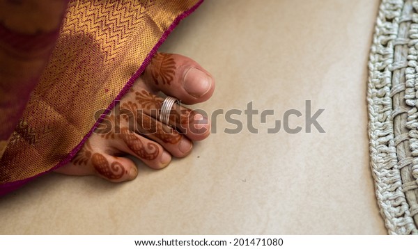 Henna covered south Indian bride\'s\
foot with a toe ring. sticking out from below the\
sari