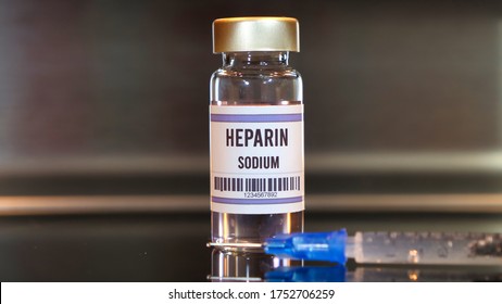 Heparin drug and syringe on black table with reflections and stainless background.