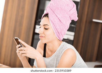 In her luminous and exceptionally spacious home, a young woman with a towel wrapped around her head dries her hair. She finds relaxation and satisfaction as she indulges in gossip and social networkin
