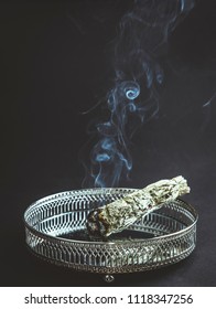 Herb bundle of dried sage smudge stick with aromatic smoke on black background. It is believed to cleanse negative energy and purify living spaces.