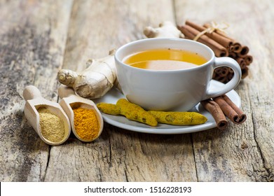 Herbal ginger and turmeric tea in white cup with ginger root, dry turmeric, cinnamon sticks and their powder. Herbal spice tea for flu cold winter days