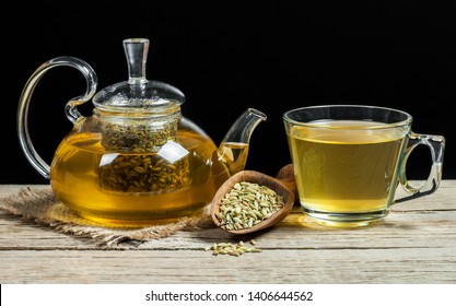 Herbal infusion fennel tea in glass cup and glass tea pot with dried fennel seeds in wooden shovel. Herbal tea alternative medicine background concept.