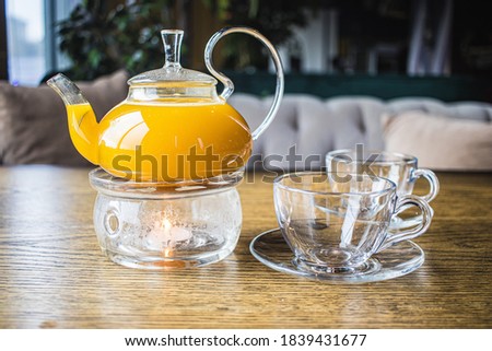 Herbal sea buckthorn tea in a transparent teapot and in a transparent glass with double heating bottom in restaurant. Concept of warmth and comfort. Mango and passion fruit tea.