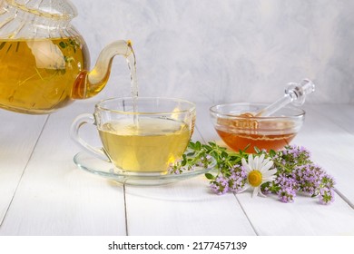 Herbal tea with chamomile and thyme in a transparent cup on a white wooden table.
