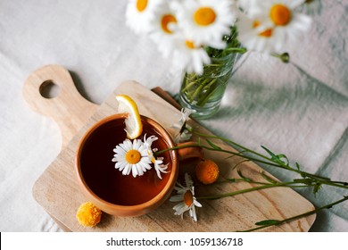 Herbal tea with fresh chamomile flowers in a ceramic mug on a linen tablecloth