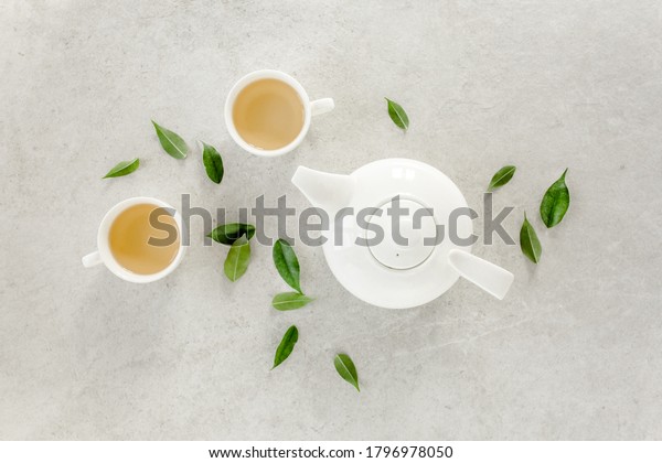 Herbal tea with two white tea
cups and teapot, with green tea leaves. Flat lay, top view. Tea
concept