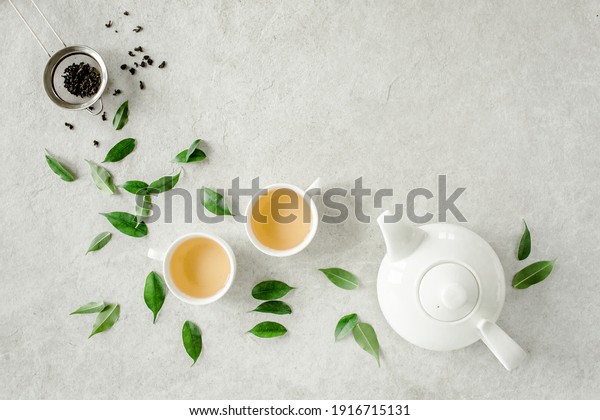 Herbal tea with two white tea\
cups and teapot, with green tea leaves. Flat lay, top view. Tea\
concept