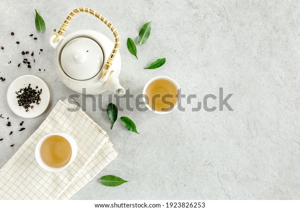 Herbal tea with two white tea\
cups and teapot, with green tea leaves. Flat lay, top view. Tea\
concept