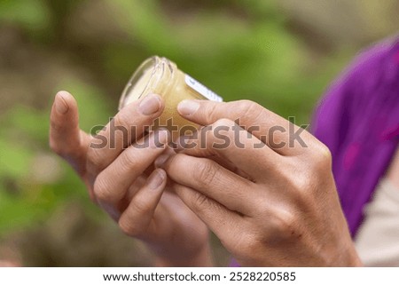 Herbalist is holding a glass jar of homemade herbal ointment, preparing to apply it. Selective focus