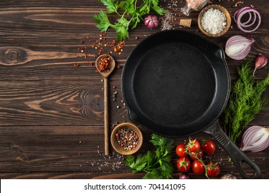 herbs and spices around cast iron skillet on wooden background.  Cooking concept. Top view. copy space