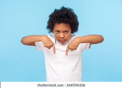 Here And Right Now! Portrait Of Angry Capricious Little Boy With Curls Pointing Down, Gesturing Below With Strict Aggressive Expression, Unruly Child Demanding To Fulfill Whim Now. Indoor Studio Shot