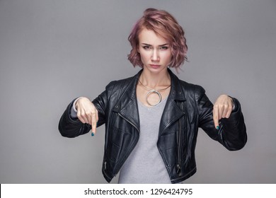 Here and right now. Portrait of bossy serious beautiful girl with short hair, makeup, casual style black leather jacket standing and looking at camera. indoor studio shot, isolated on grey background.
