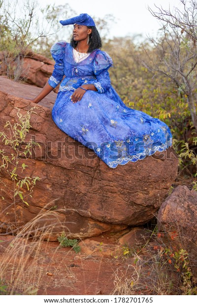 herero woman wearing a Victorian style\
dress outdoors in a village in north\
Botswana