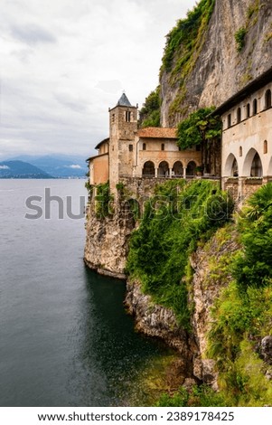 Hermitage of Santa Caterina del Sasso is historic Roman Catholic monastery Leggiuno on the Lago Maggiore in Italy. Monument and tourist attraction on a cliff above the lake on a cloudy summer day.