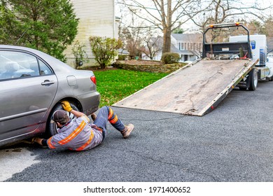 Herndon, USA - November 21, 2020: Car in driveway with tower man attaching chain to tow vehicle due to fuel leak that damaged pavement covered in cat litter to absorb the gas