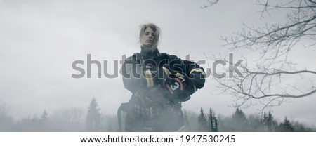 Hero shot, portrait of tired American female firefighter standing taking off her protective helmet, looking into camera