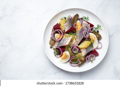herring,  pickled cucumber, beet, potato and eggs salad on white  plate, top view, copy space