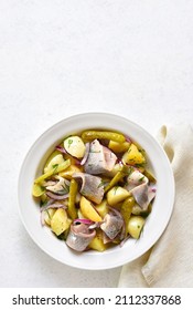 Herring salad with boiled potatoes, pickled cucumbers and red onion in bowl over light stone background with free text space. Top view, flat lay