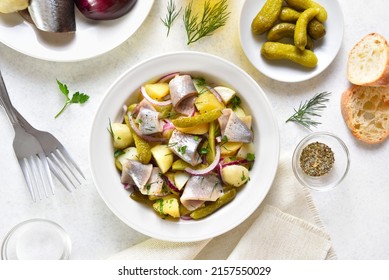 Herring salad with boiled potatoes, pickled cucumbers and red onion in bowl over light stone background. Top view, flat lay