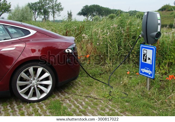 Herwijnen, The Netherlands - July 24, 2015:\
Electric charging point at a public car park in Herwijnen. The\
charging station is on the right with the Tesla Model S is plugged\
in with a cable.