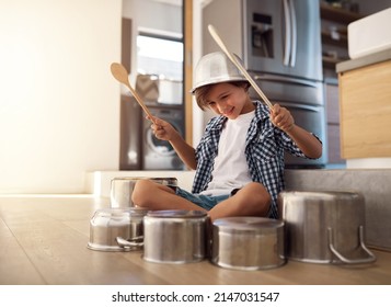 Hes a born percussionist. Shot of a happy little boy playing drums with pots on the kitchen floor while wearing a bowl on his head.