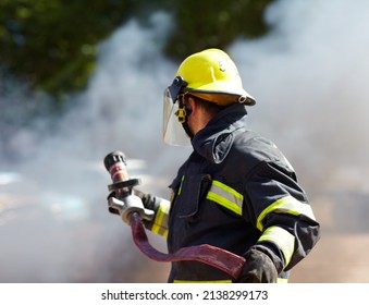 Hes got the situation under control. A caucasian fireman holding a hose and surrounded by the smoke from the fire hes just extinguished.