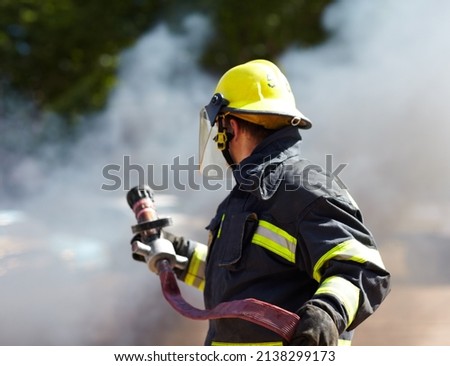 Hes got the situation under control. A caucasian fireman holding a hose and surrounded by the smoke from the fire hes just extinguished.