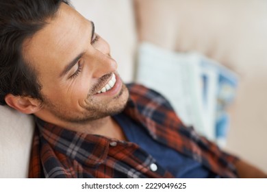 Hes a lighthearted lad. A handsome young man lying down on a sofa at home and laughing to himself. - Shutterstock ID 2229049625