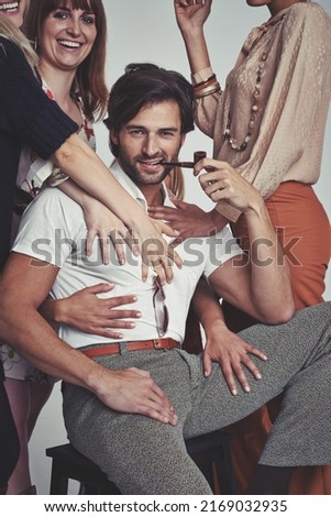 Hes one retro casanova. Studio shot of an attractive man in retro 70s wear surrounded and being touched by women while smoking his pipe.