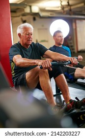 Hes Setting The Standard. Cropped Shot Of Two Men Working Out On The Rowing Machine At The Gym.