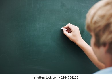 Hes writing your copy or you. Rear view of a young boy writing something on a blackboard with a piece of chalk - copyspace.