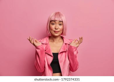 Hesitant Unsure Woman With Rosy Haircut, Shrugs Shoulders And Stands Indecisive, Hears Ridiculous Question, Feels Confused, Dressed In Pink Outfit, Cannot Understand, Poses Indoor. Life Perception